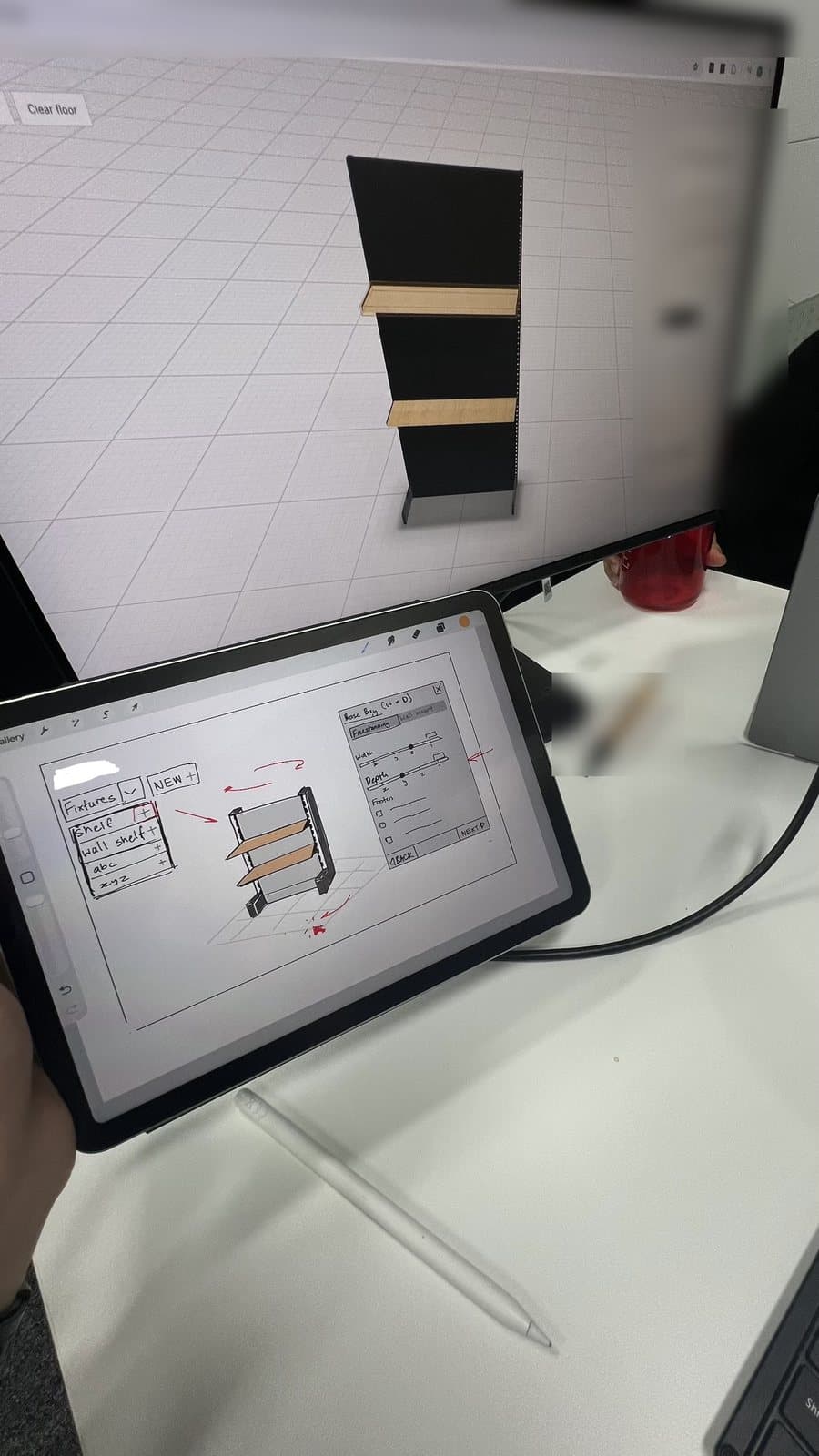 A hand-drawn configurator wireframe on a tablet, held in front of a monitor showing the first 3D build of a shelving bay